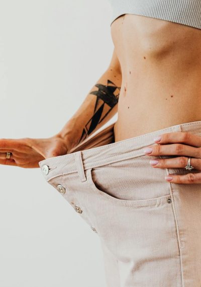 Close-up of a woman in oversized pants showcasing weight loss progress. Studio shot with neutral background.