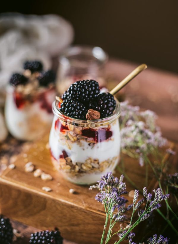 Delicious blackberry and yogurt parfait with granola served in jars and decorated with flowers.